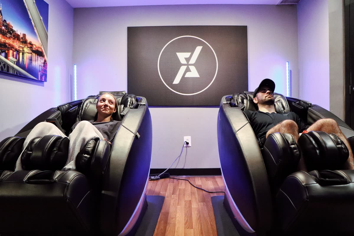 Two members reclined in Human Touch massage chairs in the recovery room at QNTM Fit Life